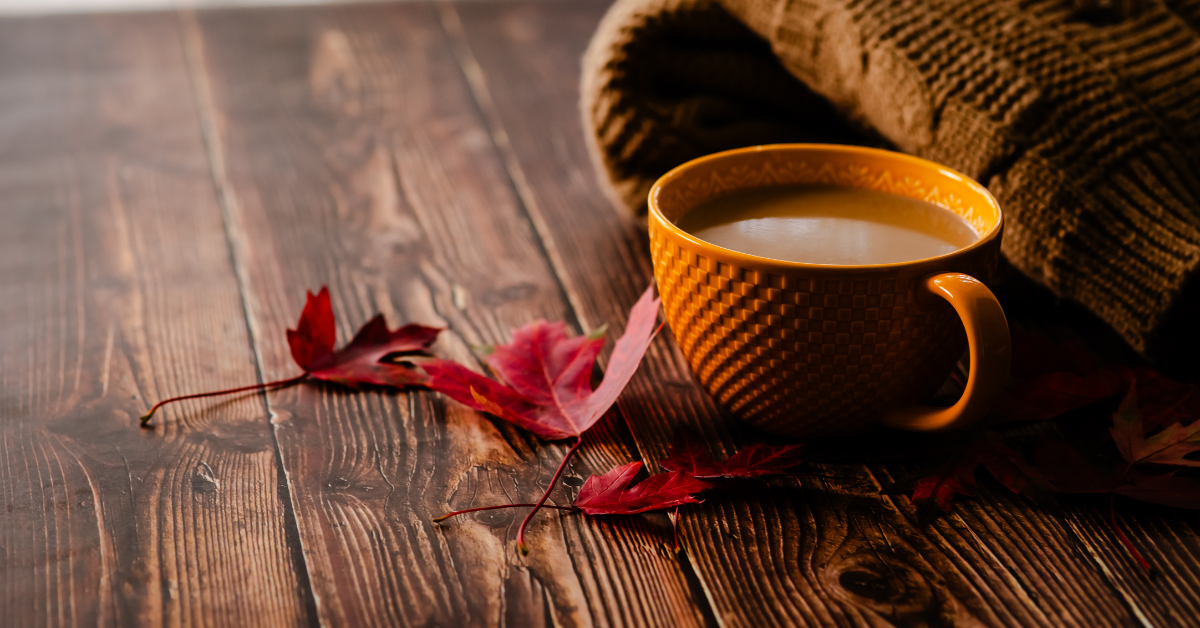 A cozy cup of coffee with a warm blanket and a red fall leaf.